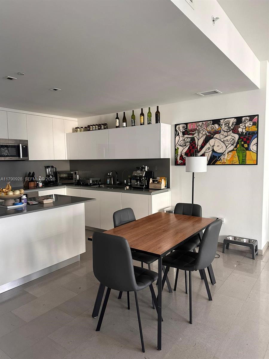 A modern kitchen with white cabinets, gray countertops, and a dining table with four chairs — 88 SW 7th St # 810, Miami FL 33130, MIAMI, FL