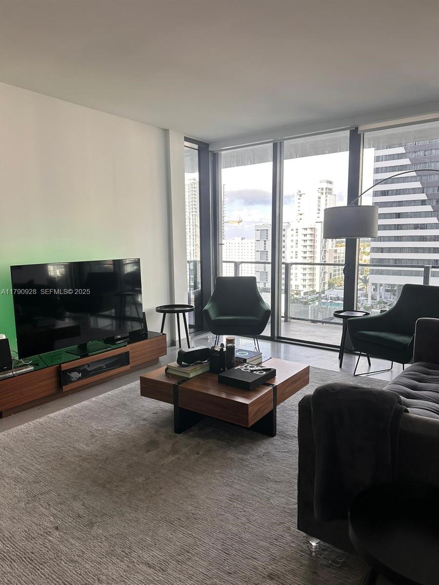 A modern living room features a wooden coffee table, two green armchairs, and floor-to-ceiling windows — 88 SW 7th St # 810, Miami FL 33130, MIAMI, FL