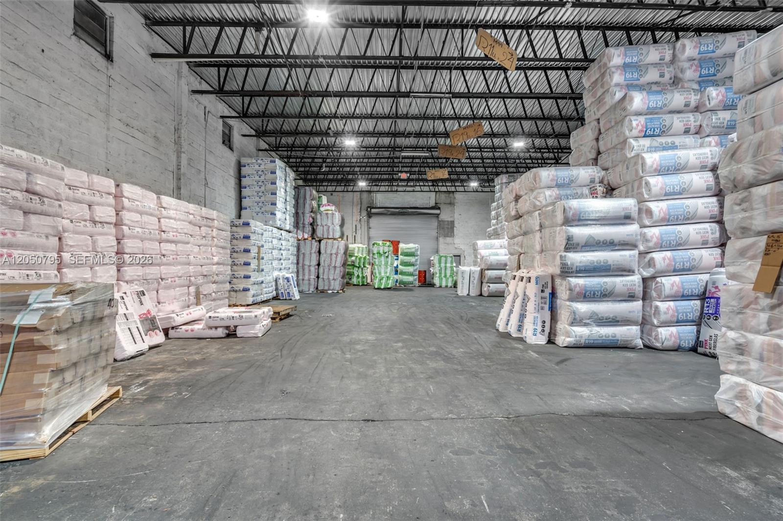 A large warehouse interior features high ceilings and stacks of insulation material on pallets — 7440 NW 66th St, Miami FL 33166, MIAMI, FL
