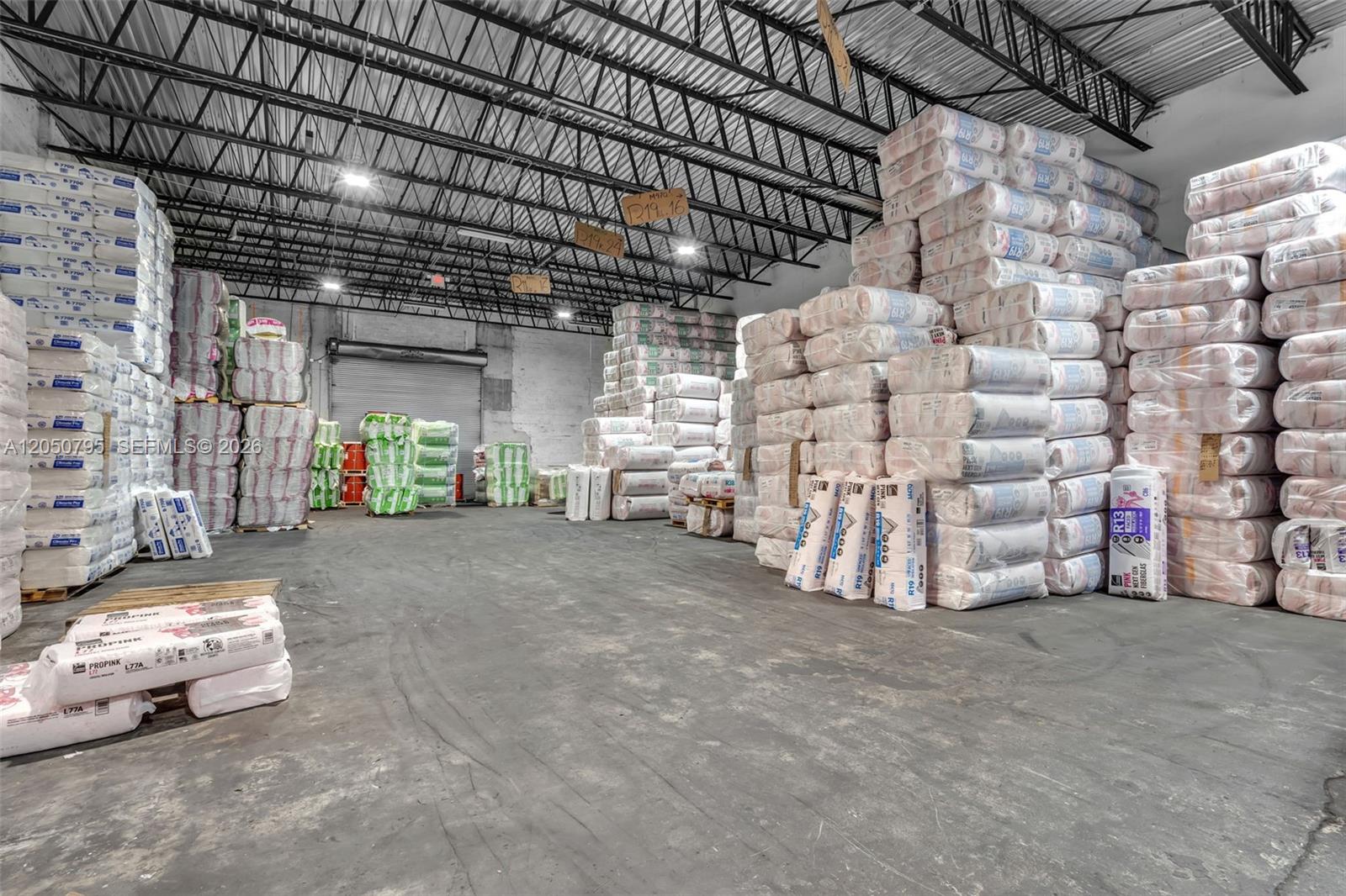 A large warehouse interior features high ceilings and stacks of insulation material on pallets — 7440 NW 66th St, Miami FL 33166, MIAMI, FL