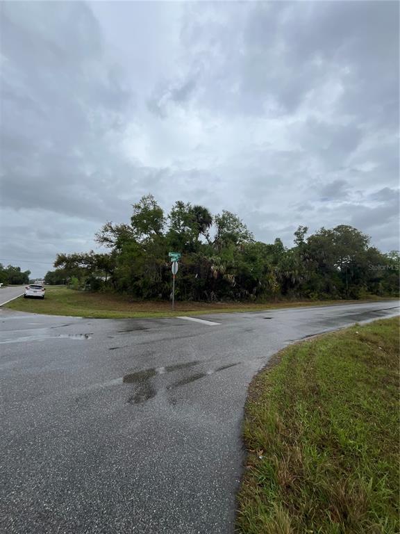 A paved intersection meets a wooded, undeveloped lot under a cloudy sky — 15010 ELWOOD AVENUE, PORT CHARLOTTE, FL