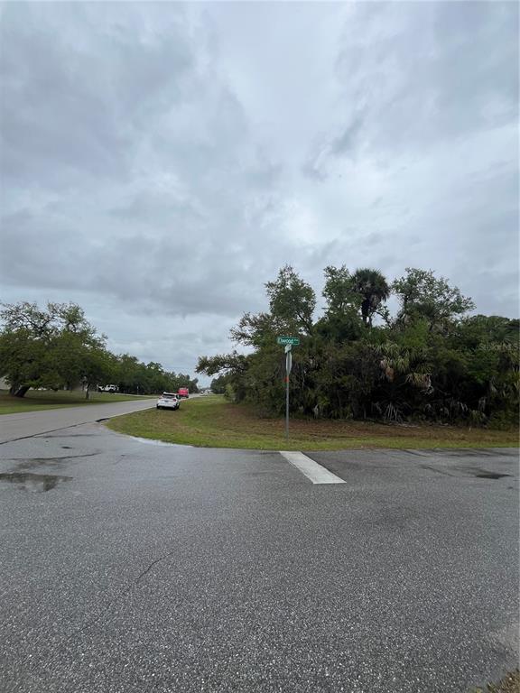 A paved road intersection features a street sign and a wooded lot under a cloudy sky — 15010 ELWOOD AVENUE, PORT CHARLOTTE, FL