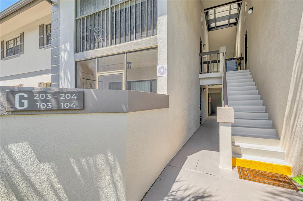 An exterior view of a multi-story apartment building with a concrete staircase and unit signage — 1515 FORREST NELSON BOULEVARD UNIT G104, PORT CHARLOTTE, FL