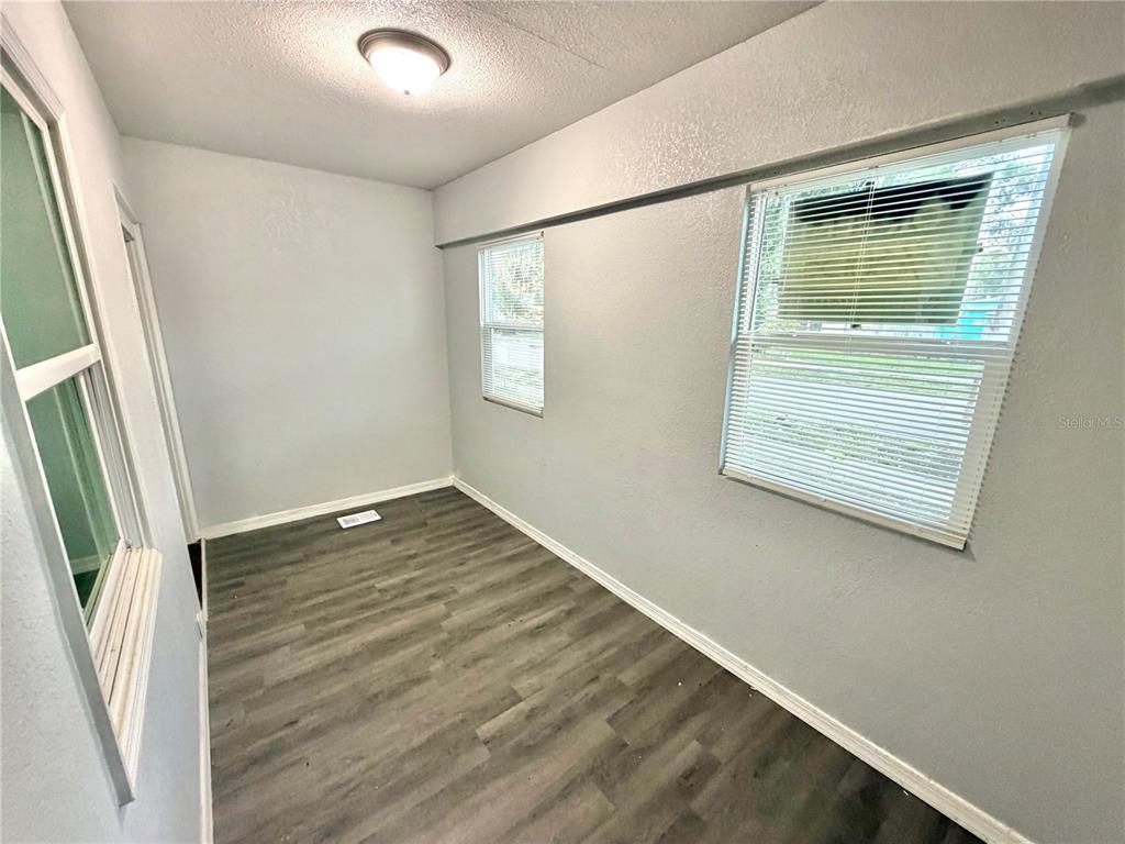 An empty room features gray walls, wood-look flooring, and three windows with white blinds — 4700 10TH AVENUE S, ST PETERSBURG, FL