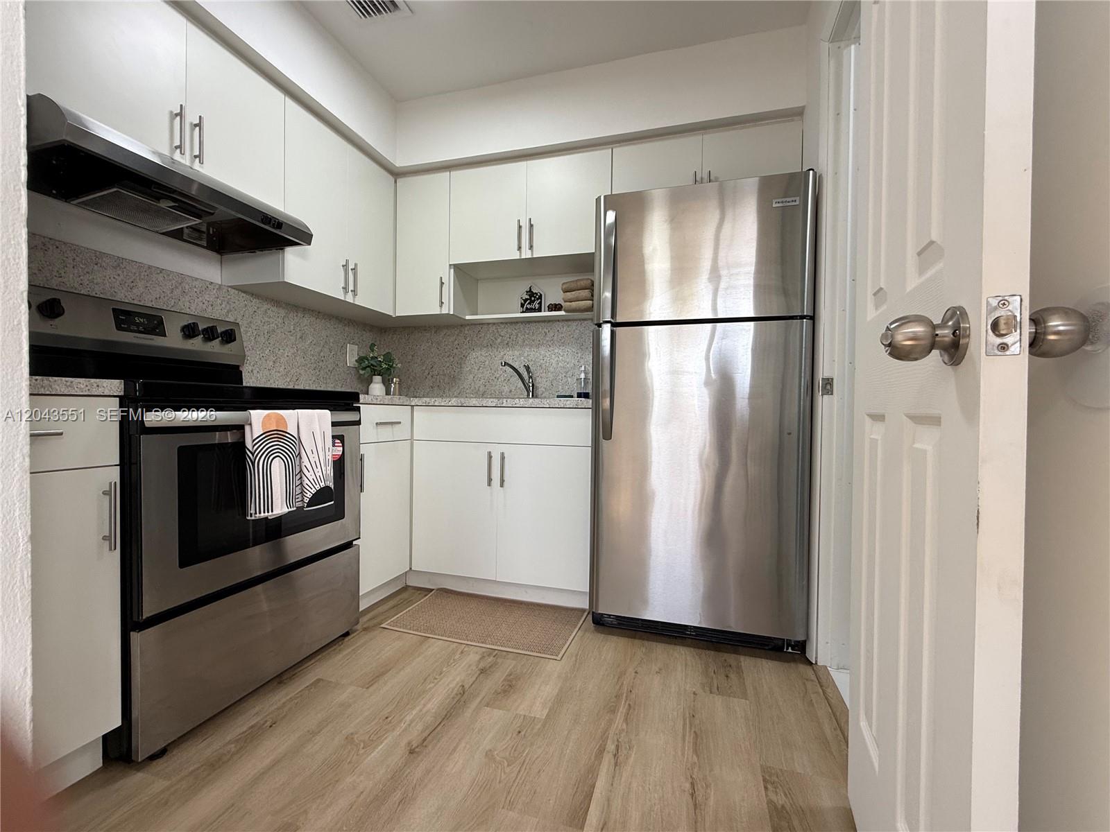A small kitchen features white cabinets, stainless steel appliances, and wood-look flooring — 8860 SW 32nd st, Miami FL 33165, MIAMI, FL
