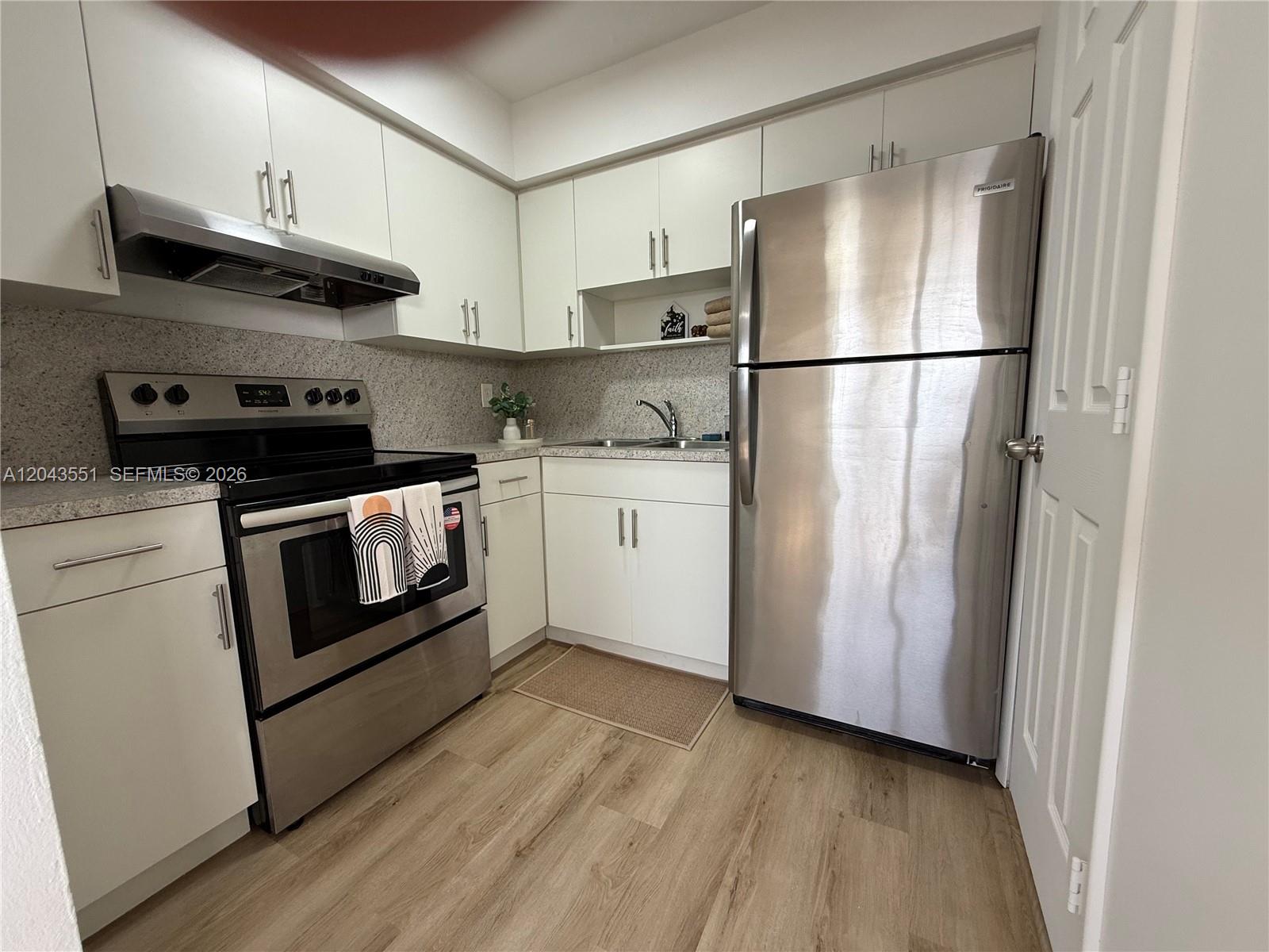 A kitchen features white cabinets, stainless steel appliances, and light wood-look flooring — 8860 SW 32nd st, Miami FL 33165, MIAMI, FL