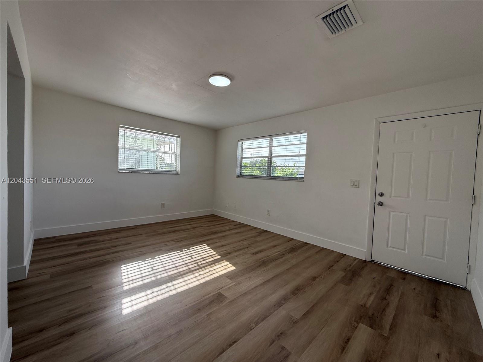 An empty room features white walls, wood-look flooring, two windows, and a white door — 8860 SW 32nd st, Miami FL 33165, MIAMI, FL