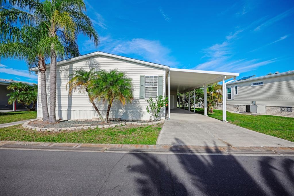 A single-story manufactured home with light siding, a palm tree, and a concrete carport — 2100 KINGS HIGHWAY UNIT 364, PORT CHARLOTTE, FL