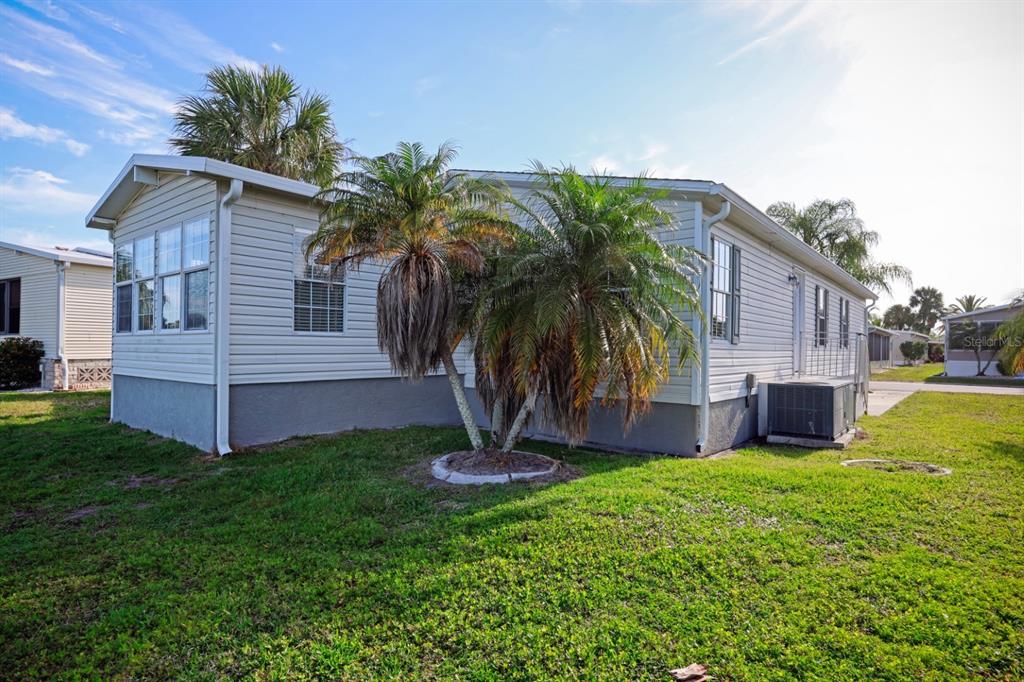 Exterior view of a light-colored manufactured home with palm trees and a central air unit — 2100 KINGS HIGHWAY UNIT 364, PORT CHARLOTTE, FL