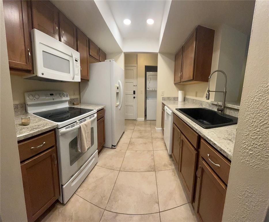 A galley kitchen features wood cabinets, granite countertops, white appliances, and a black sink — 308 PALM COAST PARKWAY NE UNIT 203, PALM COAST, FL
