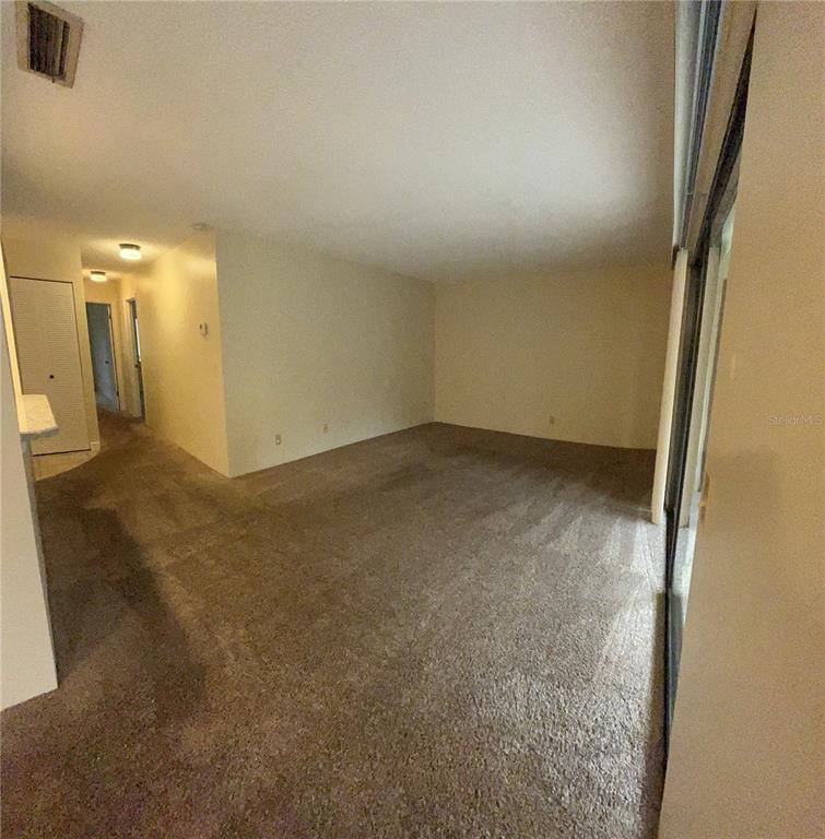 An empty living room with beige carpet, off-white walls, and a sliding glass door — 308 PALM COAST PARKWAY NE UNIT 203, PALM COAST, FL