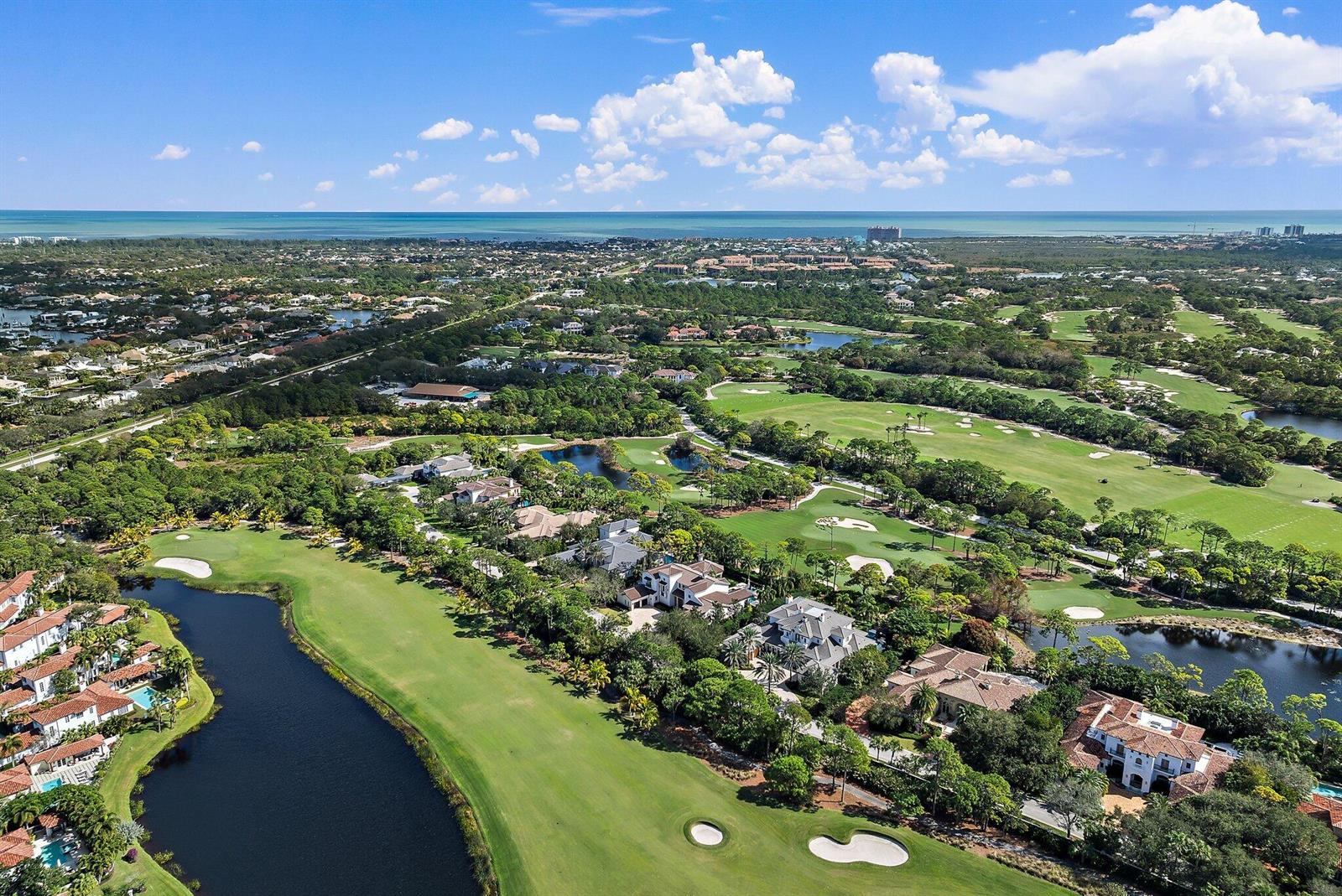 An aerial view shows luxury homes bordering a golf course with ponds and the ocean beyond — 135 W Bears Club Drive, Jupiter FL 33477, JUPITER, FL