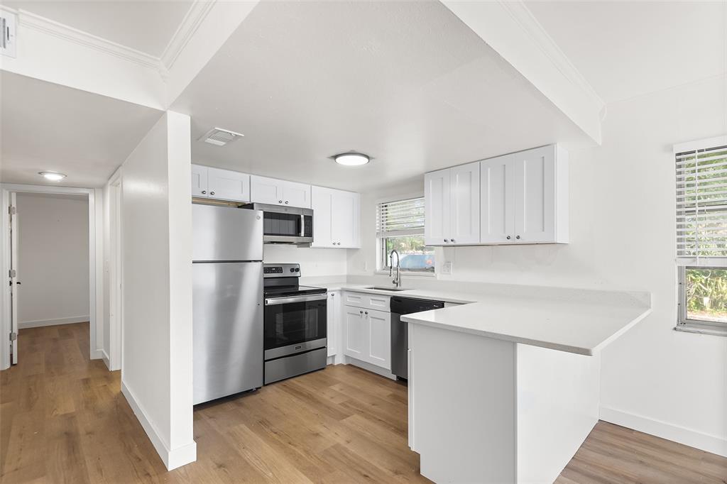 A kitchen features white cabinets, stainless steel appliances, and light wood-look flooring — 555 62ND STREET S UNIT 110, ST PETERSBURG, FL