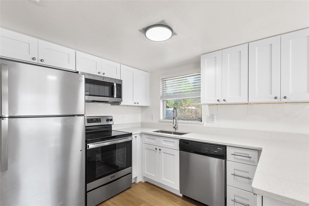 A kitchen features white cabinets, stainless steel appliances, a window, and light-colored countertops — 555 62ND STREET S UNIT 110, ST PETERSBURG, FL