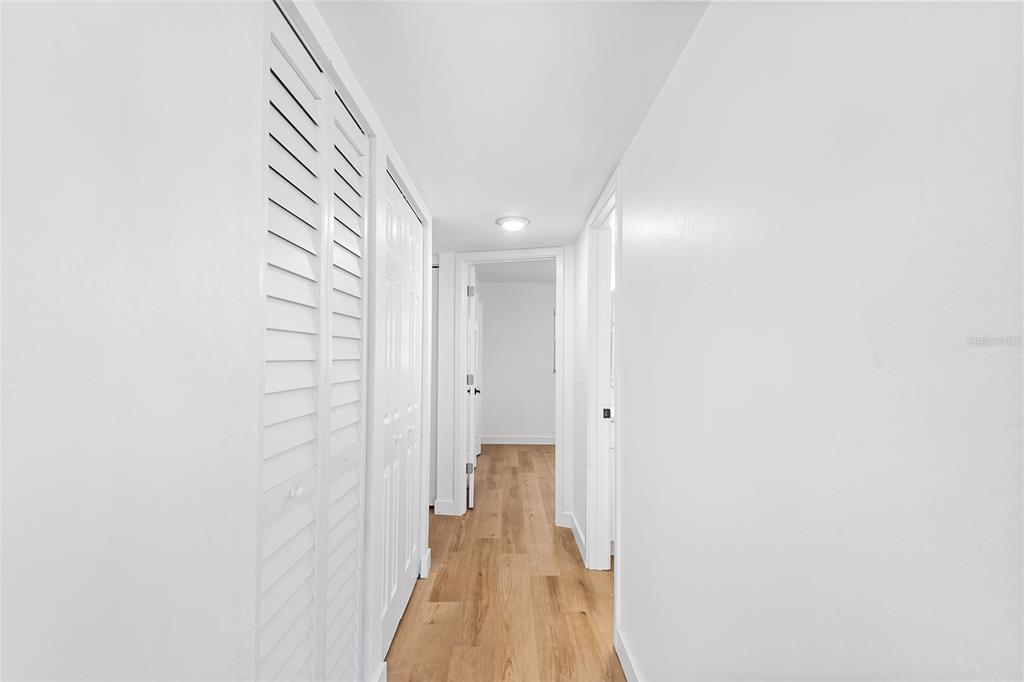 A hallway with white walls, light wood flooring, and white louvered closet doors — 555 62ND STREET S UNIT 110, ST PETERSBURG, FL