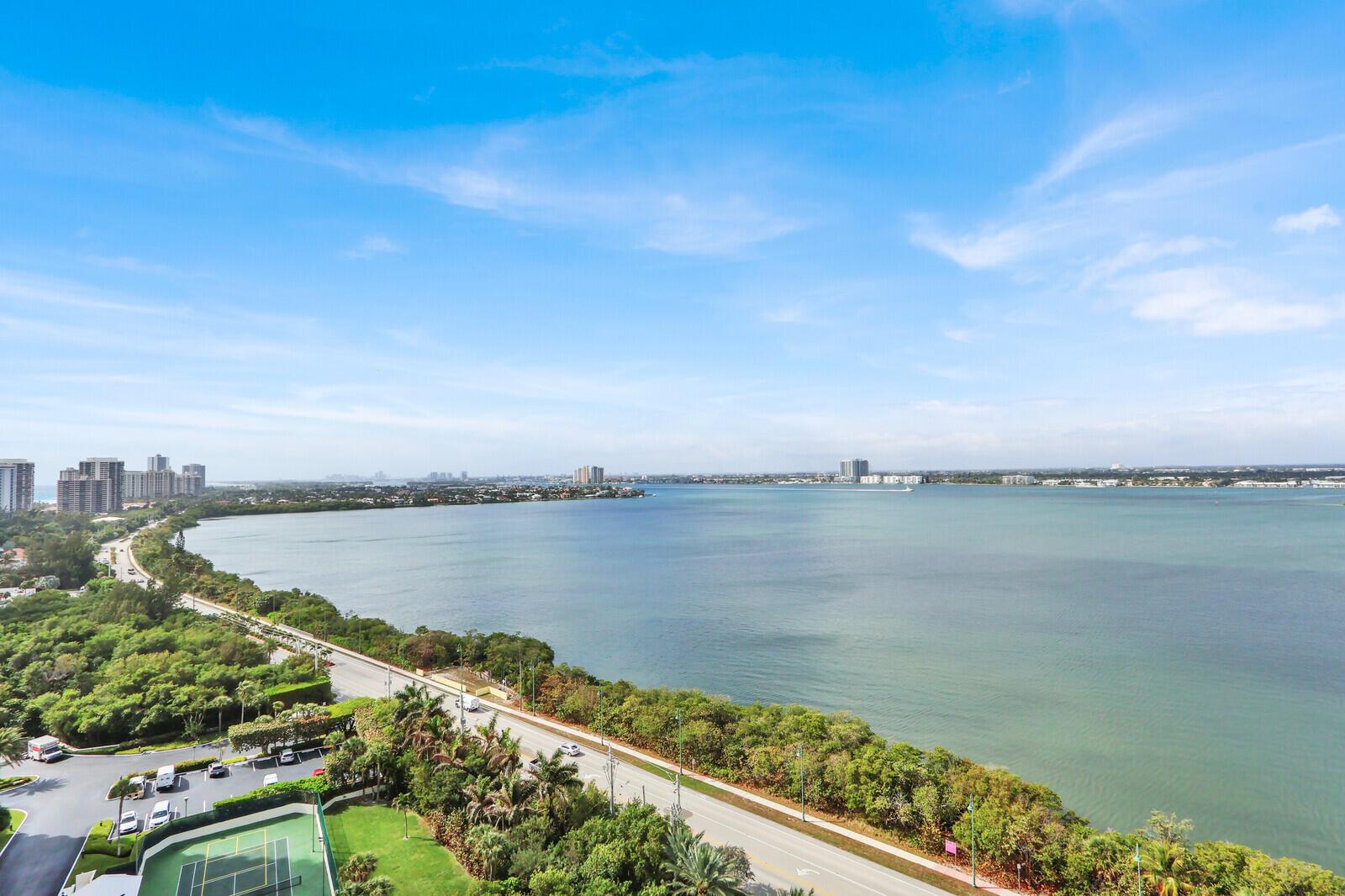 An elevated view of a coastal road, lush greenery, a tennis court, and a large bay — 5380 N Ocean Drive # 18a, Singer Island FL 33404, SINGER ISLAND, FL