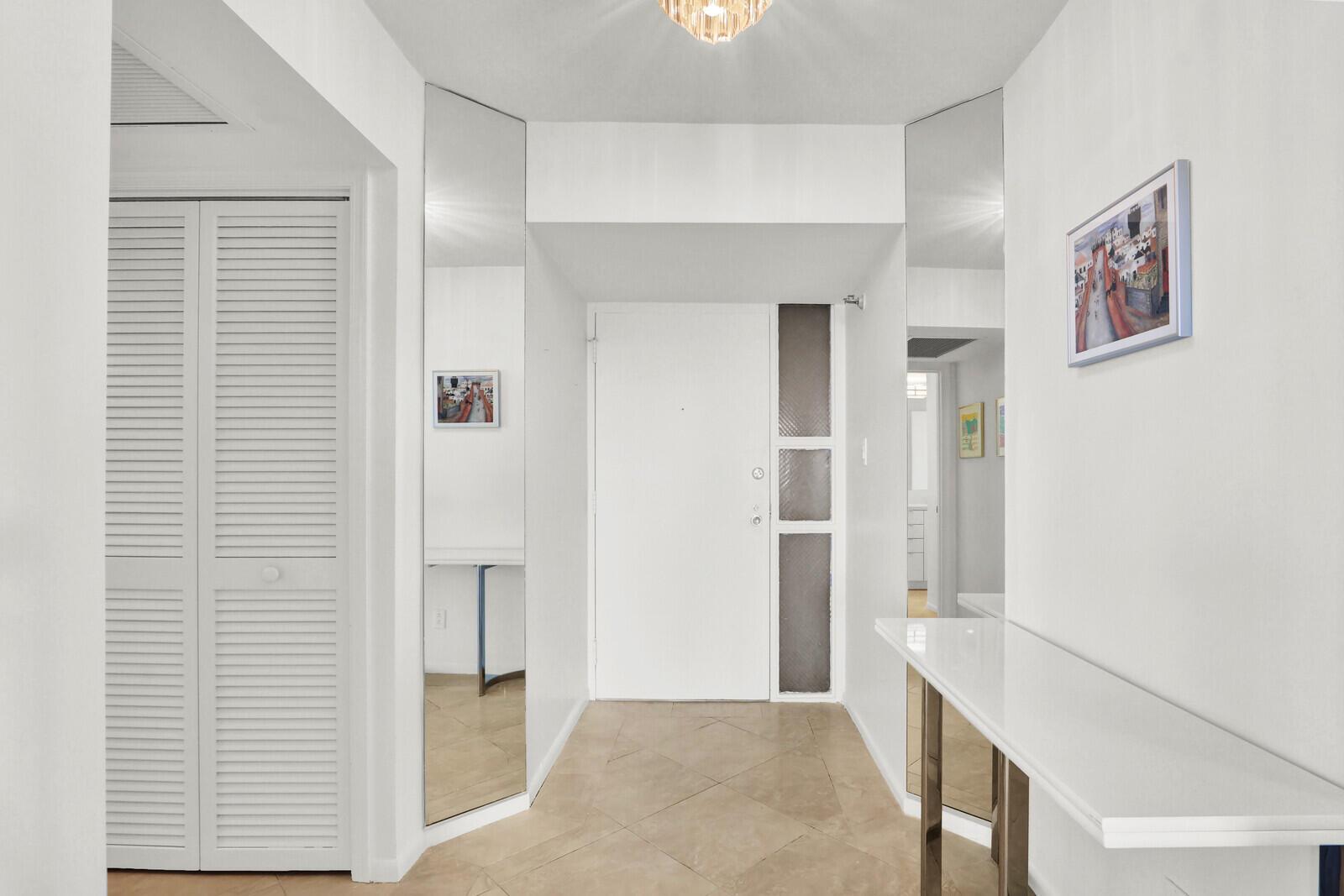 A bright entryway features white walls, tiled floors, a white door, and mirrored wall panels — 5380 N Ocean Drive # 18a, Singer Island FL 33404, SINGER ISLAND, FL