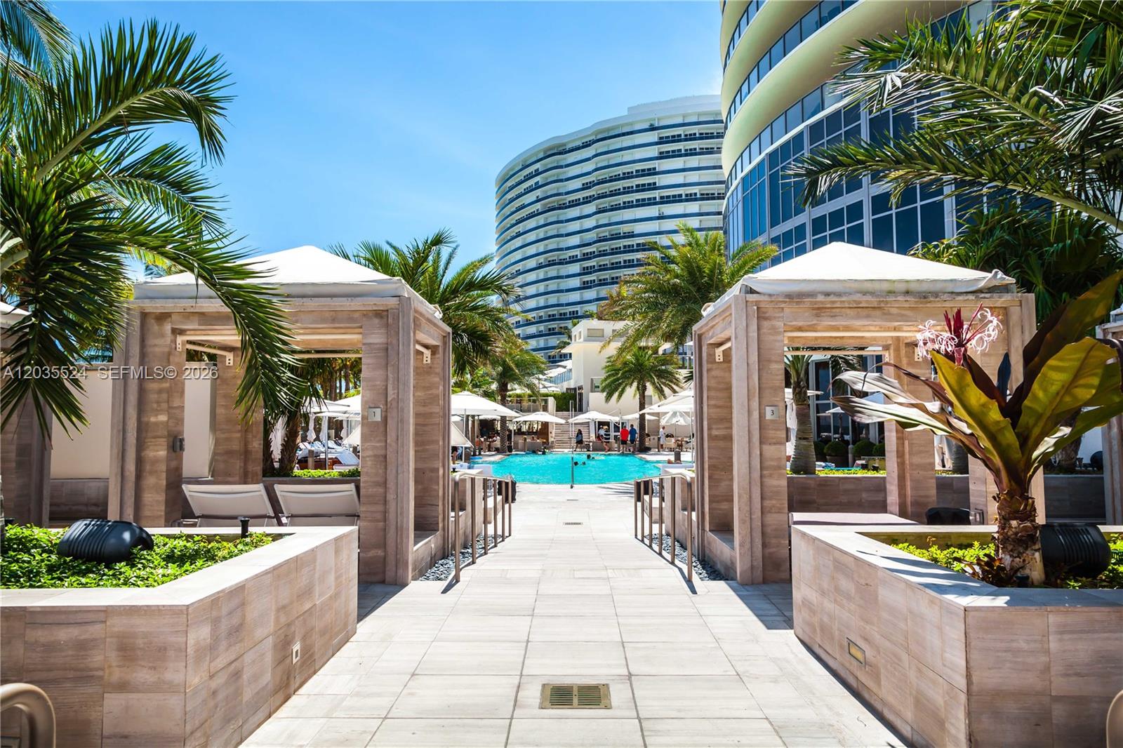 A paved walkway leads between two poolside cabanas toward a swimming pool and tall buildings — 9703 Collins Ave, Bal Harbour FL 33154, BAL HARBOUR, FL