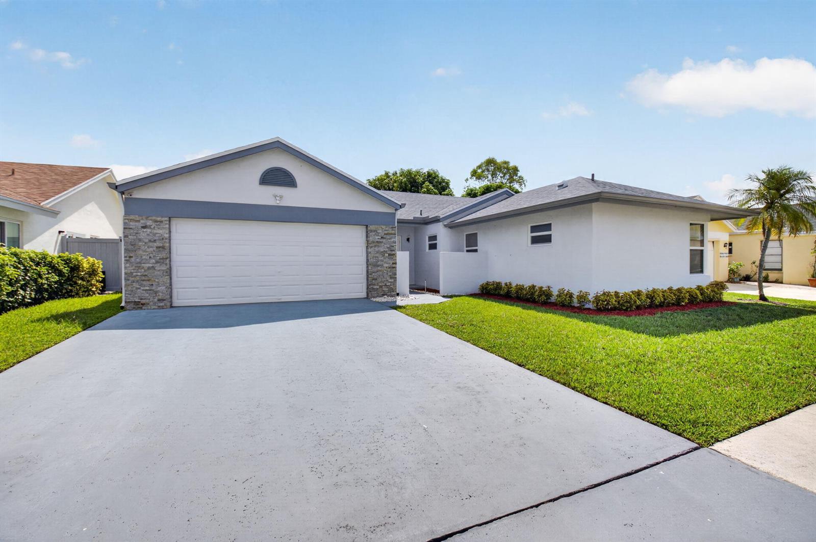 A single-story house with a gray driveway, stone accents, and a white garage door — 21070 Woodspring Avenue, Boca Raton FL 33428, BOCA RATON, FL
