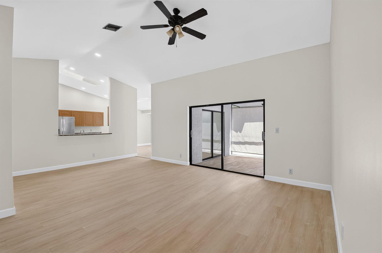 A spacious living room features light wood-look flooring, a vaulted ceiling, and sliding glass doors — 21070 Woodspring Avenue, Boca Raton FL 33428, BOCA RATON, FL