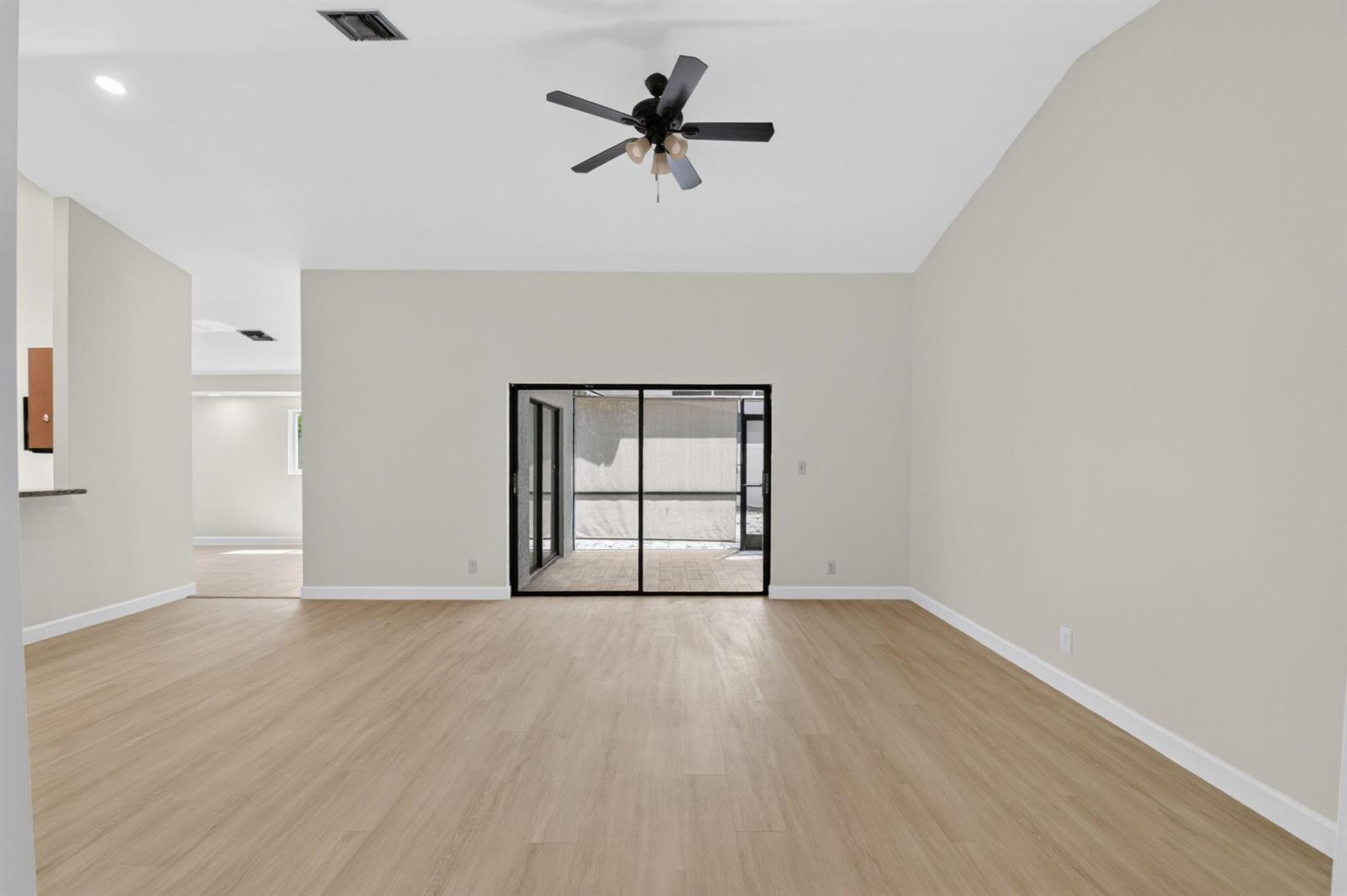 An empty living room features light wood-look flooring, a vaulted ceiling with a fan, and sliding doors — 21070 Woodspring Avenue, Boca Raton FL 33428, BOCA RATON, FL