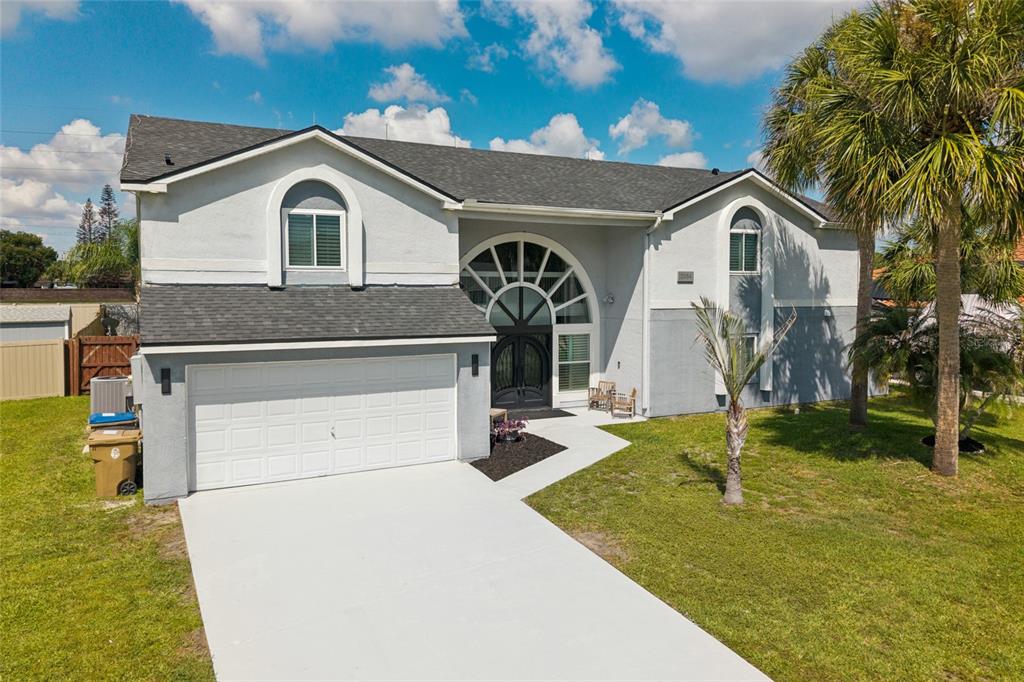 A two-story house with a white garage, arched windows, and a palm tree in front — 2484 ALBANY DRIVE, KISSIMMEE, FL
