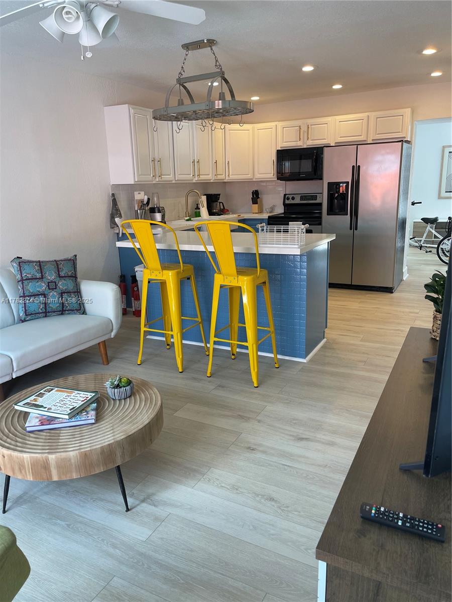 A kitchen with blue tile, yellow bar stools, and white cabinets opens to a living area — 1560 NE 145th St # 2, Miami FL 33161, MIAMI, FL