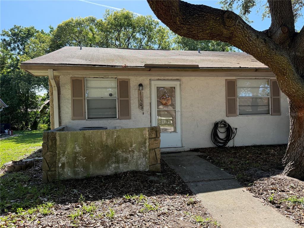 A single-story house exterior features a stucco facade, a concrete walkway, and a stone wall — 1150 CHENEY HIGHWAY UNIT H, TITUSVILLE, FL