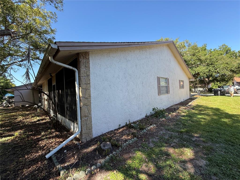 The side exterior of a house features white stucco walls, stone accents, and a downspout — 1150 CHENEY HIGHWAY UNIT H, TITUSVILLE, FL