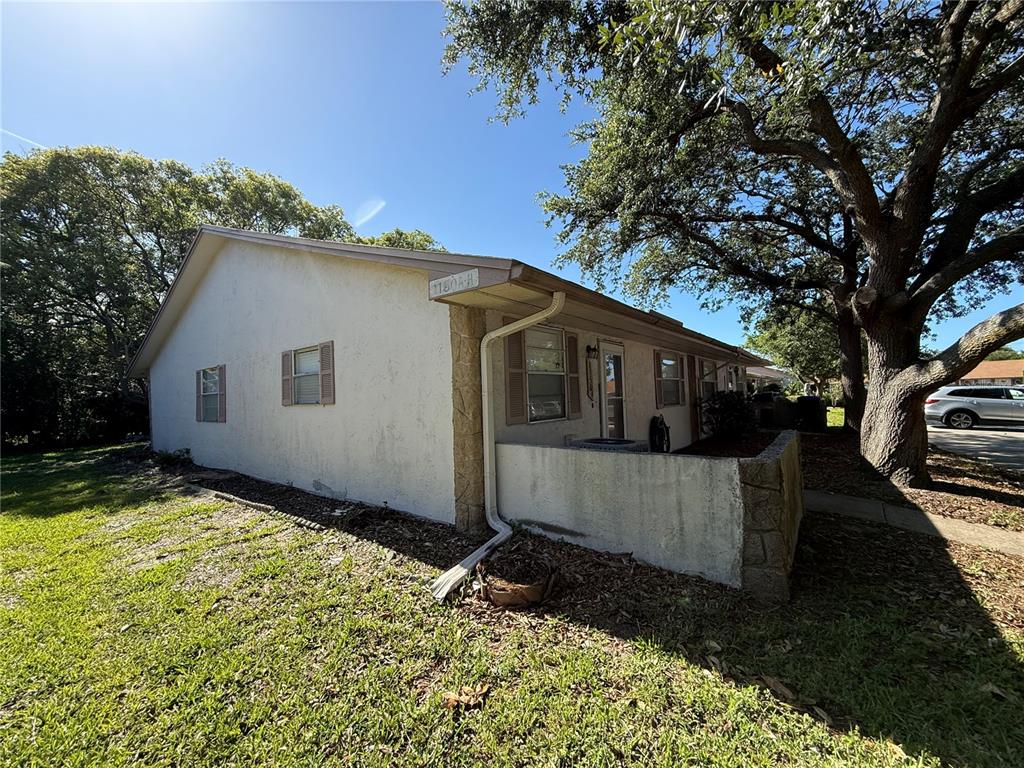 The exterior of a single-story residential building features stucco walls, a concrete patio, and trees — 1150 CHENEY HIGHWAY UNIT H, TITUSVILLE, FL