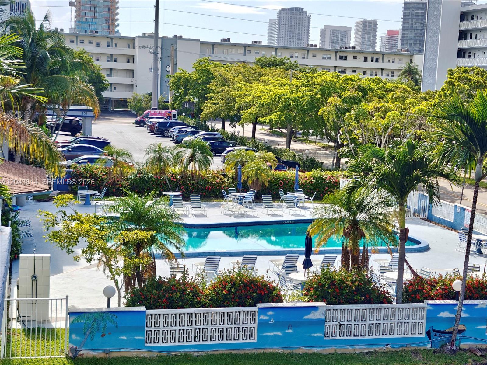 An elevated view of a swimming pool area with lounge chairs, palm trees, and parking — 400 NE 12th Ave # 306, Hallandale Beach FL 33009, HALLANDALE BEACH, FL