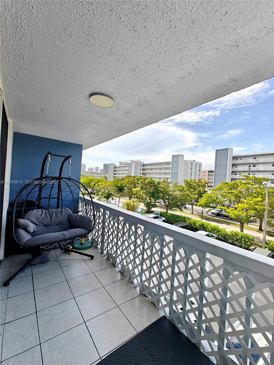 A balcony features a hanging egg chair, tiled flooring, and a white lattice railing — 400 NE 12th Ave # 306, Hallandale Beach FL 33009, HALLANDALE BEACH, FL