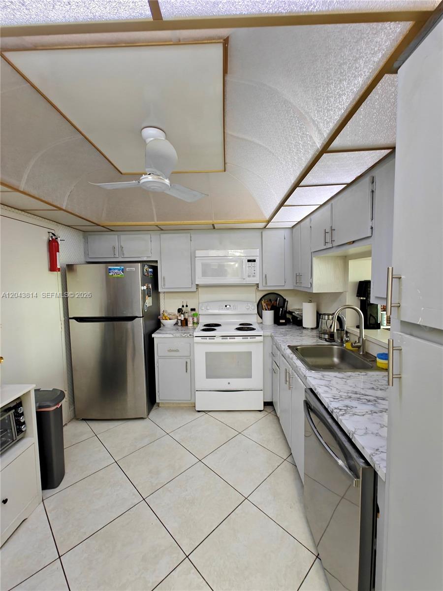 A kitchen features light gray cabinets, white appliances, a stainless steel refrigerator, and marble-patterned countertops — 400 NE 12th Ave # 306, Hallandale Beach FL 33009, HALLANDALE BEACH, FL