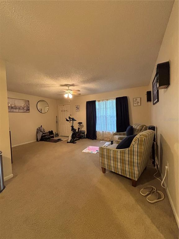 A living room features beige carpeting, a stationary bike, and a plaid armchair — 2690 CORAL LANDINGS BOULEVARD UNIT 127, PALM HARBOR, FL
