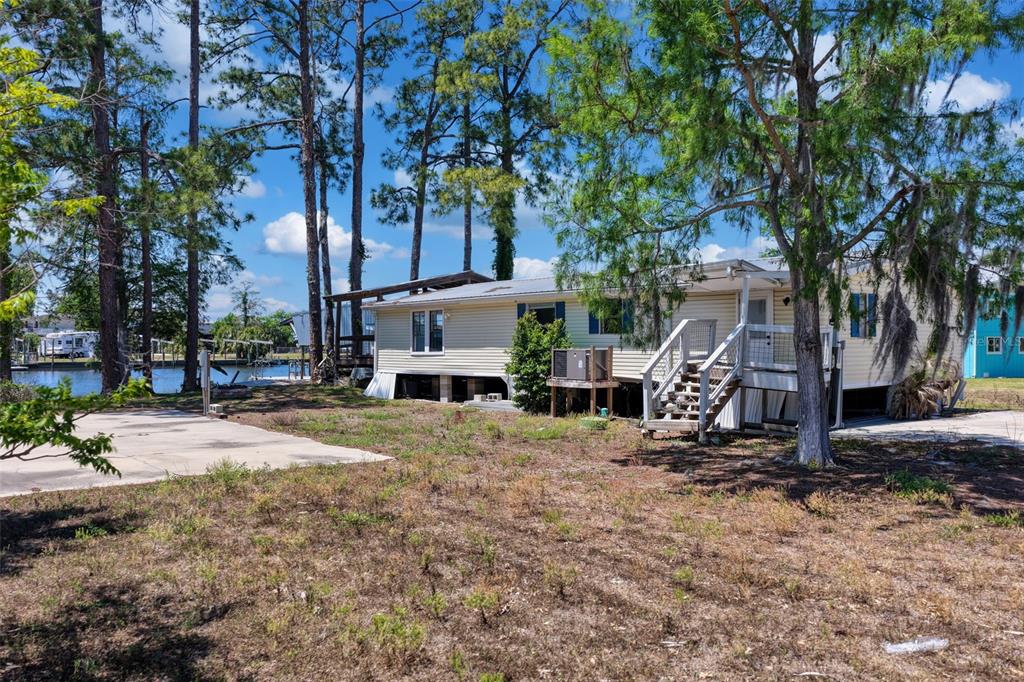 A light-colored mobile home sits on a lot with trees and a nearby canal — 53 SE 241ST STREET, SUWANNEE, FL