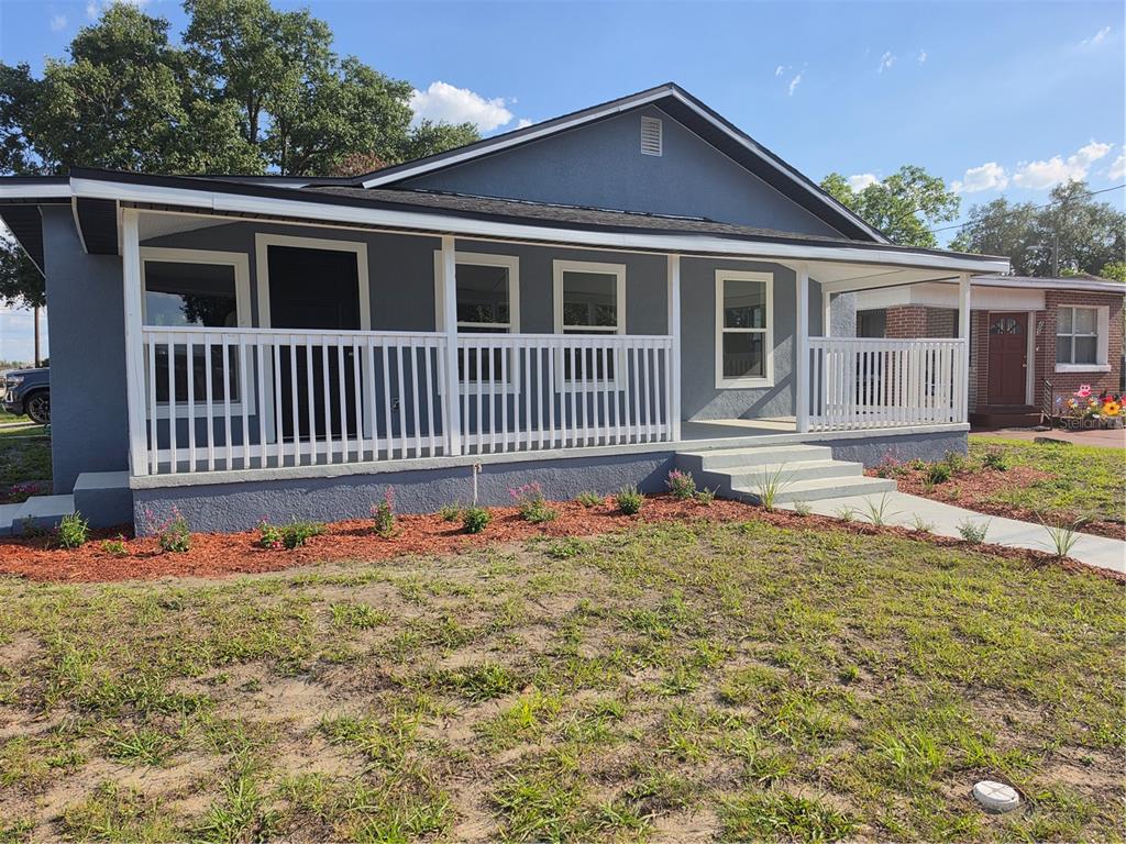 A blue house with a white porch and railing sits behind a landscaped front yard — 201 DR J A WILTSHIRE AVENUE W, LAKE WALES, FL