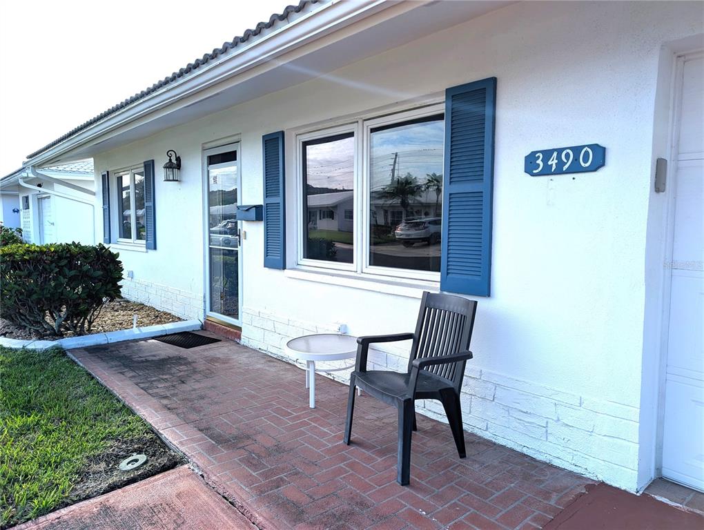 A white house exterior features a brick patio, blue shutters, and a black plastic chair — 3490 101ST TERRACE N, PINELLAS PARK, FL