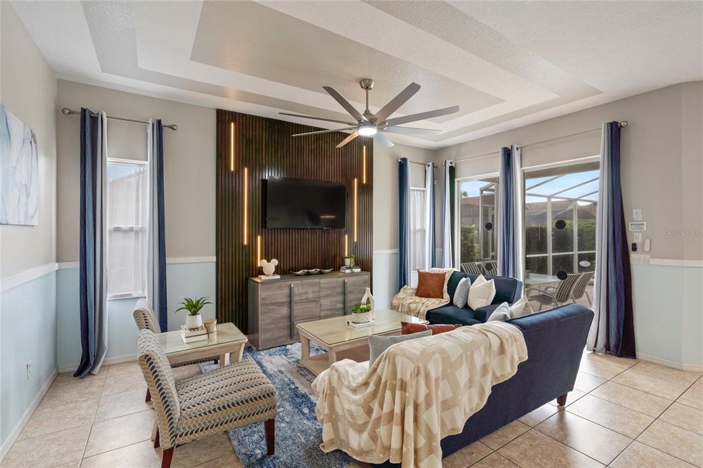 A living room features a wood-slat accent wall with integrated lighting, a ceiling fan, and furniture — 730 BRUNELLO DRIVE, DAVENPORT, FL