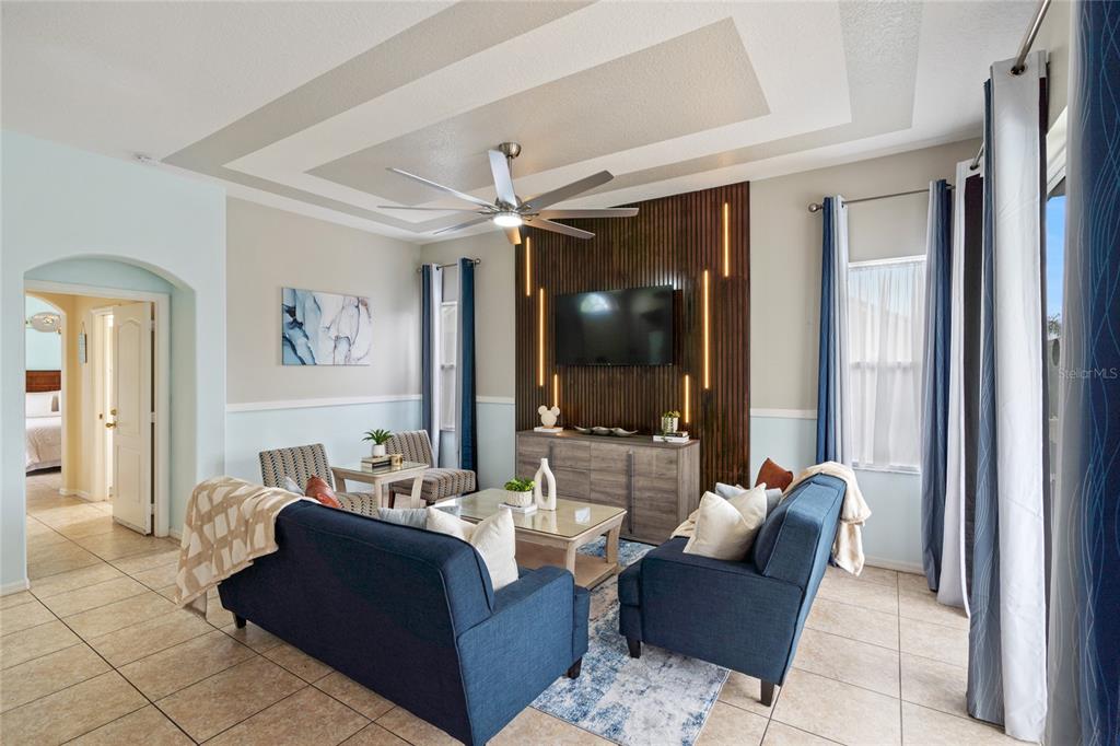 A living room features blue sofas, a wood-slat accent wall with a television, and tile flooring — 730 BRUNELLO DRIVE, DAVENPORT, FL