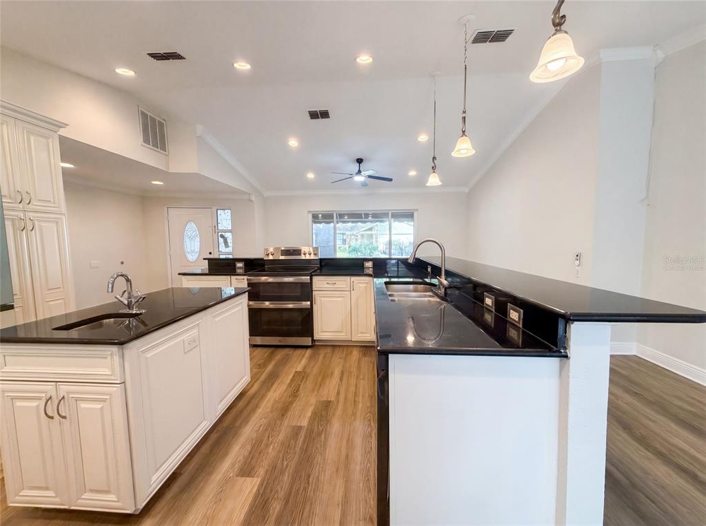 A kitchen features white cabinets, black countertops, a center island, and wood-look flooring — 37 OSPREY STREET, SAFETY HARBOR, FL