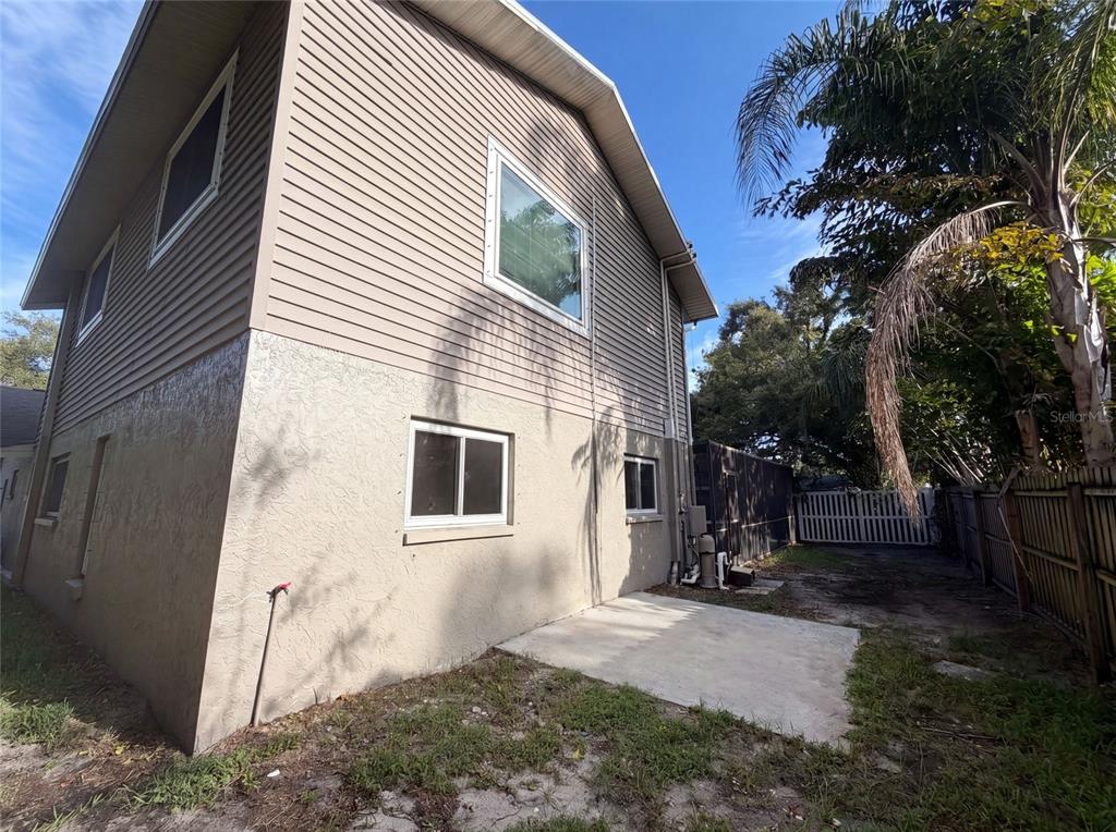 The exterior side of a two-story house features tan siding, stucco walls, and a concrete patio — 37 OSPREY STREET, SAFETY HARBOR, FL