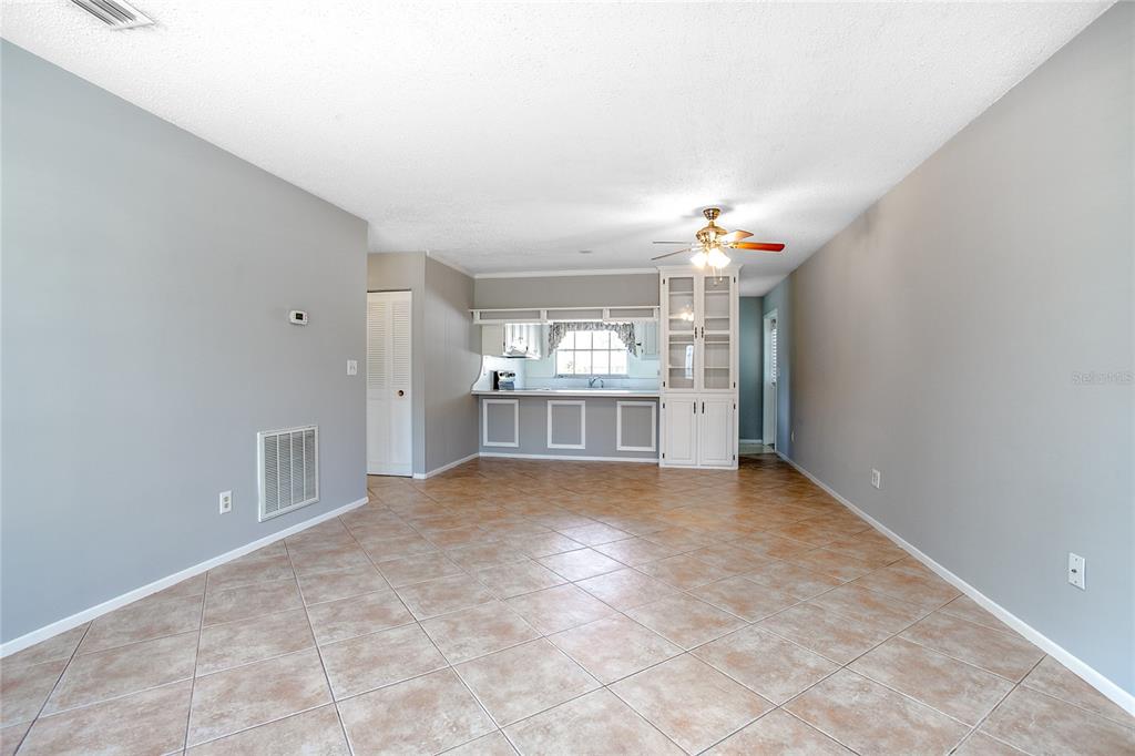 A living room with light gray walls and tan tile flooring leads to a kitchen — 135 W MINNESOTA AVENUE UNIT 10, DELAND, FL