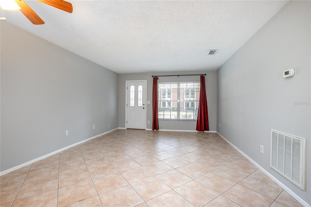 A living room with light gray walls, tile flooring, a front door, and a window — 135 W MINNESOTA AVENUE UNIT 10, DELAND, FL
