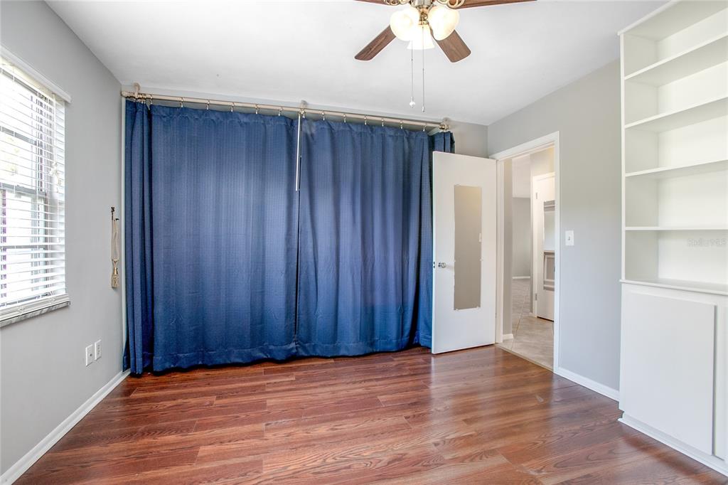 A room with dark wood flooring, blue curtains, a ceiling fan, and built-in white shelving — 135 W MINNESOTA AVENUE UNIT 10, DELAND, FL