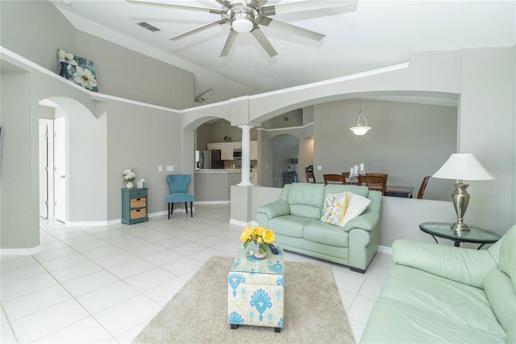 A living room with light green sofas, tile flooring, and an arched entryway to the kitchen — 1057 SOARING EAGLE LANE, KISSIMMEE, FL