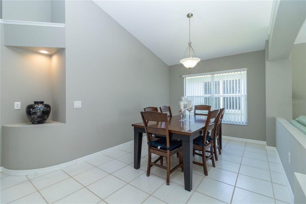 A dining room features a wooden table, six chairs, tile flooring, and a vaulted ceiling — 1057 SOARING EAGLE LANE, KISSIMMEE, FL