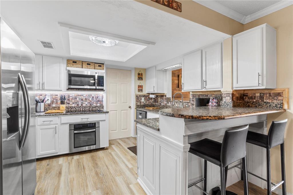 A kitchen features white cabinets, granite countertops, stainless steel appliances, and a breakfast bar — 7533 SW 108TH PLACE, OCALA, FL