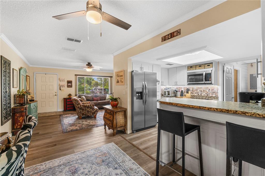 An open-concept living room and kitchen featuring wood-look flooring, stainless steel appliances, and bar seating — 7533 SW 108TH PLACE, OCALA, FL