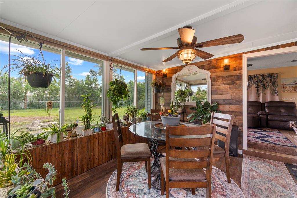 A sunroom features a glass dining table, wood-paneled walls, a ceiling fan, and many plants — 7533 SW 108TH PLACE, OCALA, FL