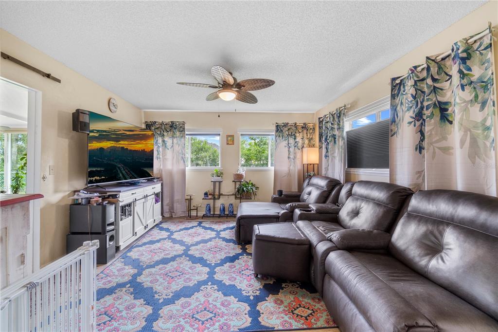 A living room features a large television, a dark leather sectional, and a patterned rug — 7533 SW 108TH PLACE, OCALA, FL